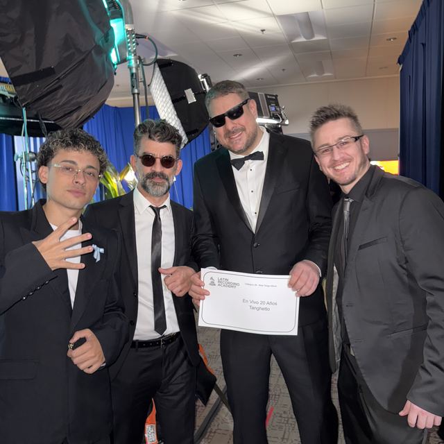 Cuatro músicos en el backstage, uno con un diploma en la mano