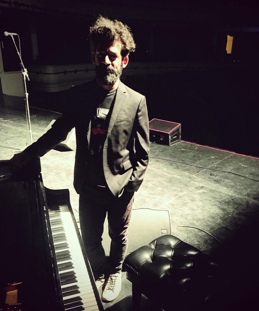 Antonio de pie junto al piano en un escenario a oscuras